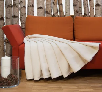 Couverture en peluche dans un ton naturel clair, étendue sur un canapé